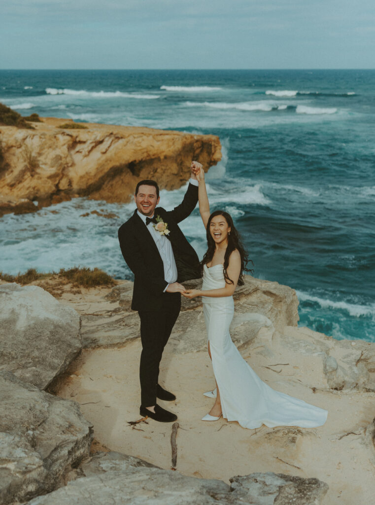 Bride and groom holding hands and smiling after their Shipwreck Beach elopement with ocean waves behind them
