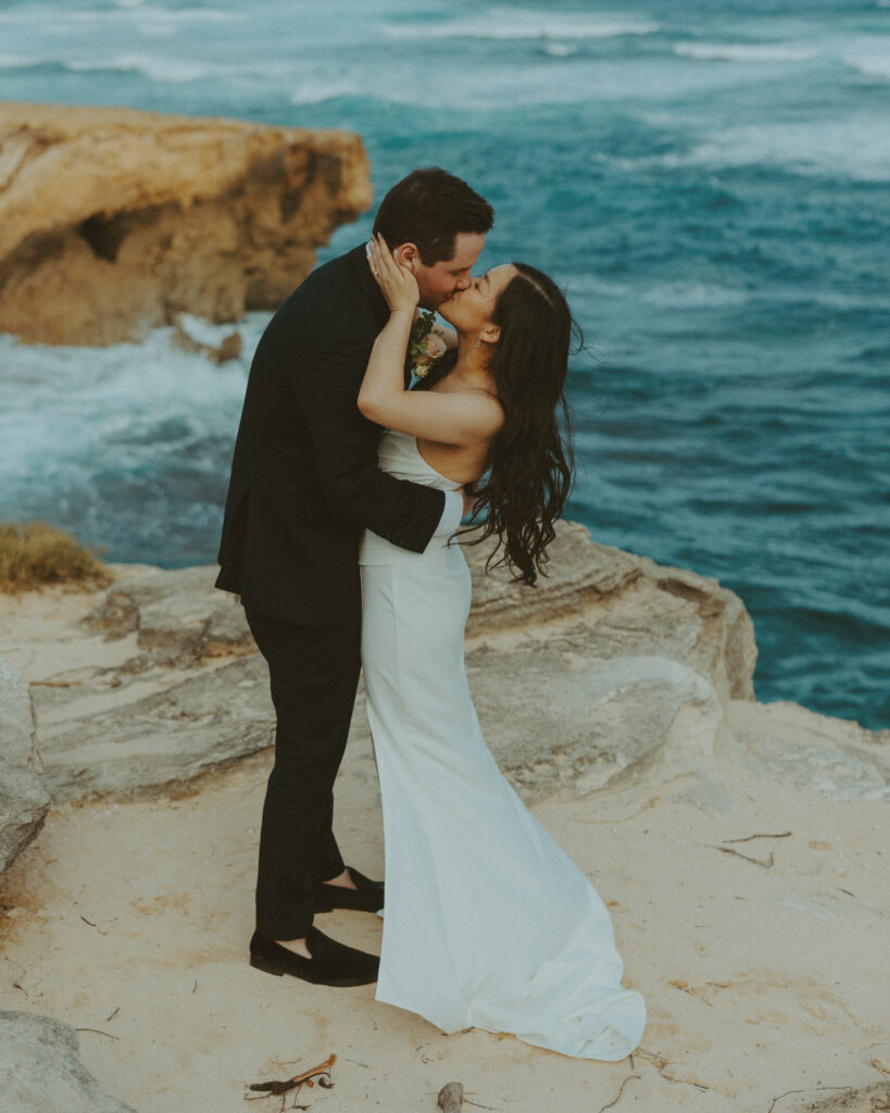 Bride and groom holding hands and smiling after their Shipwreck Beach elopement with ocean waves behind them
