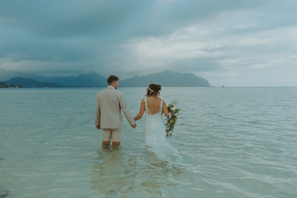 Bride and groom standing in shallow ocean water during a beach wedding ceremony