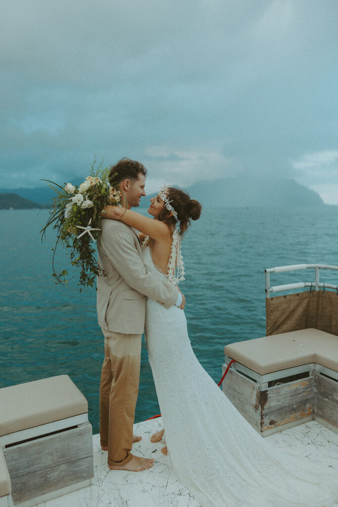 Newlyweds embracing on a boat with ocean views behind them
