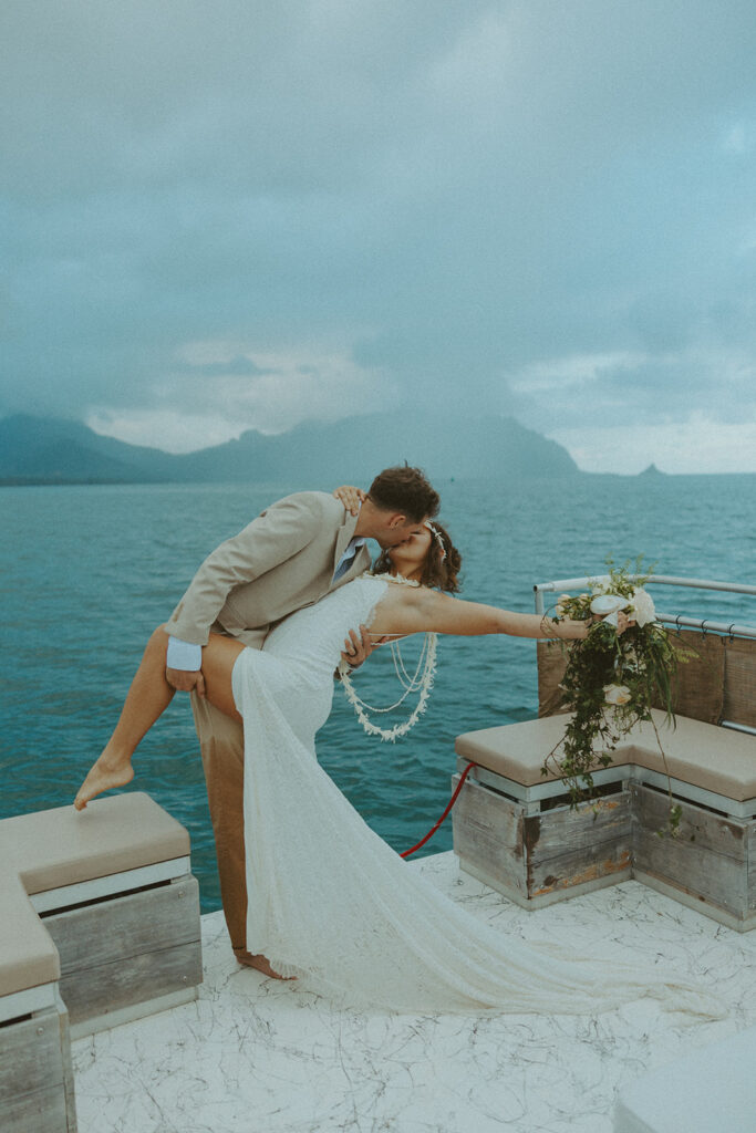 Newlyweds embracing on a boat with ocean views behind them
