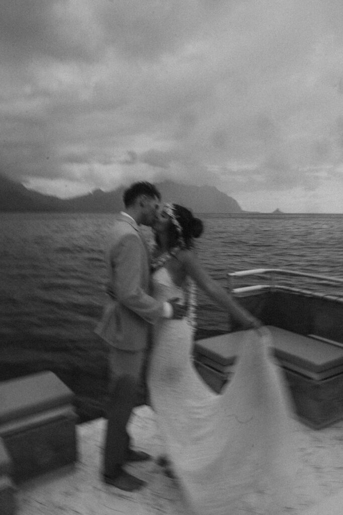 Newlyweds embracing on a boat with ocean views behind them