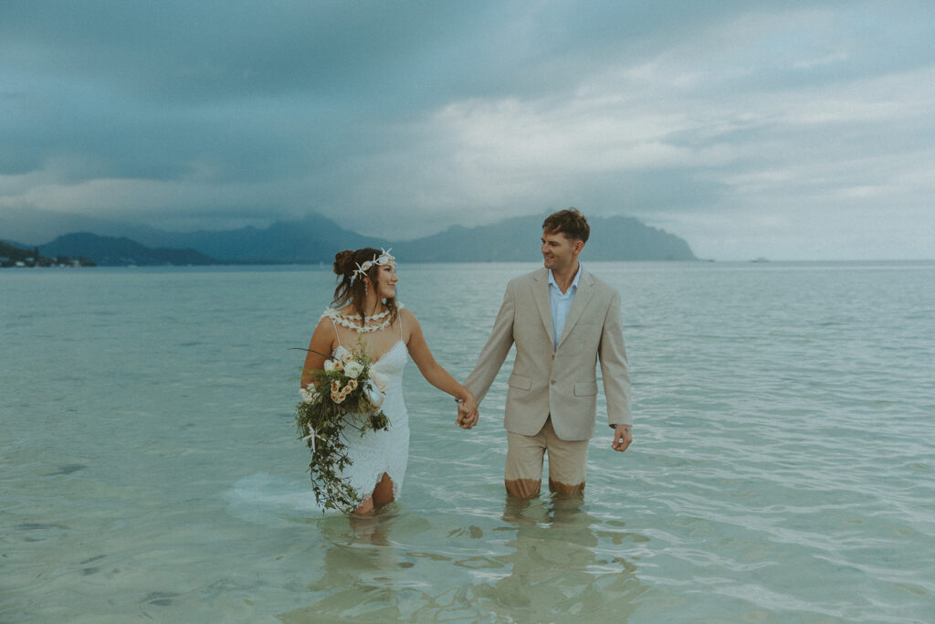 Couple holding hands in the water with mountains in the background
