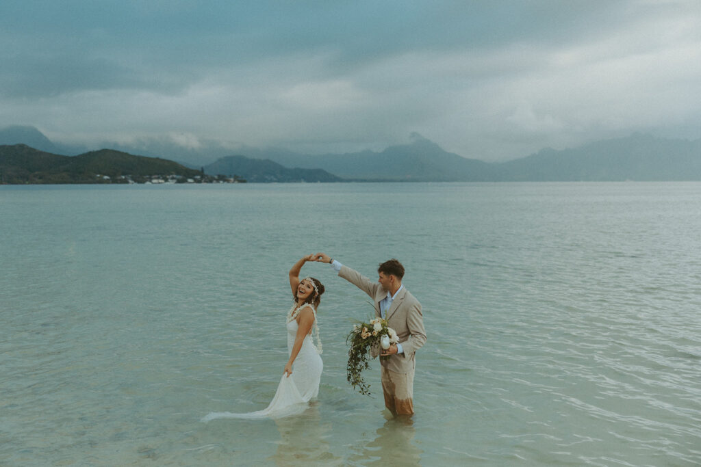 Couple holding hands in the water with mountains in the background
