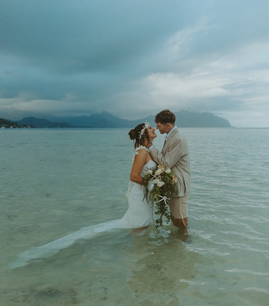 Bride and groom standing in shallow ocean water during a beach wedding ceremony
