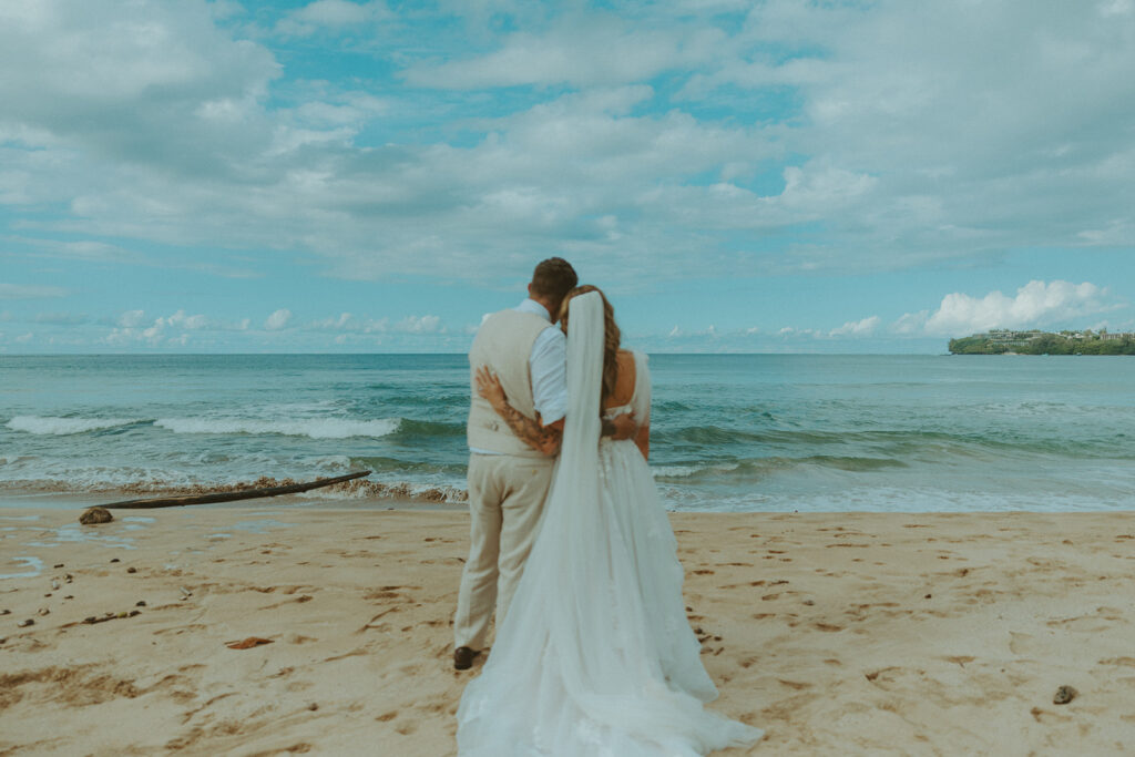 Newlyweds walking along a scenic coastal overlook in Kauai at sunset.
