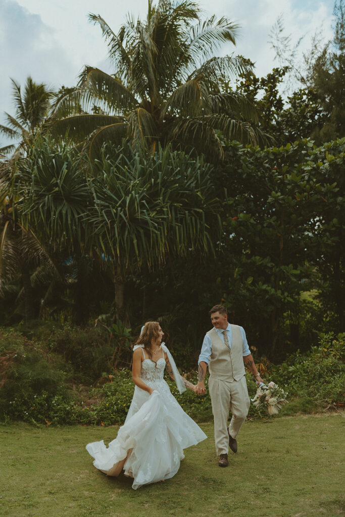 Newlyweds walking along a scenic coastal overlook in Kauai at sunset.
