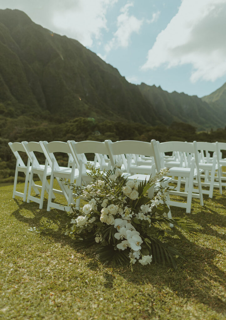 Outdoor wedding ceremony setup with white chairs and floral ceremony arch
